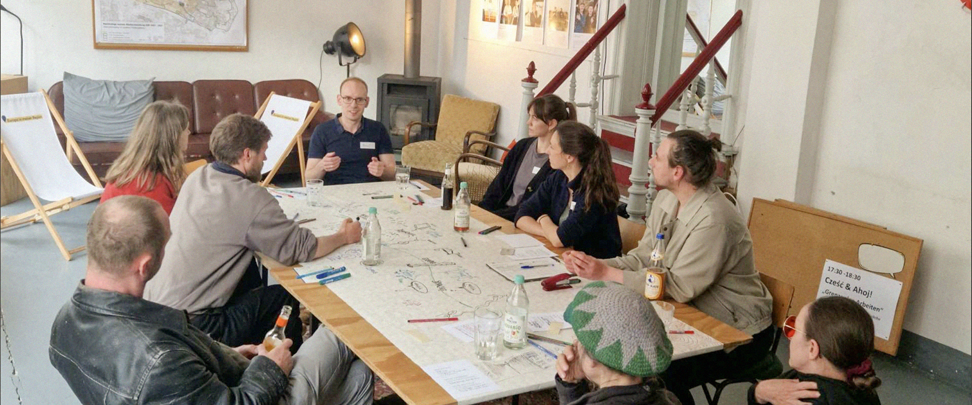 Mehrere Personen sitzen bei einem Workshop von AHOJ gemeinsam an einem großen Tisch und tauschen sich aus.